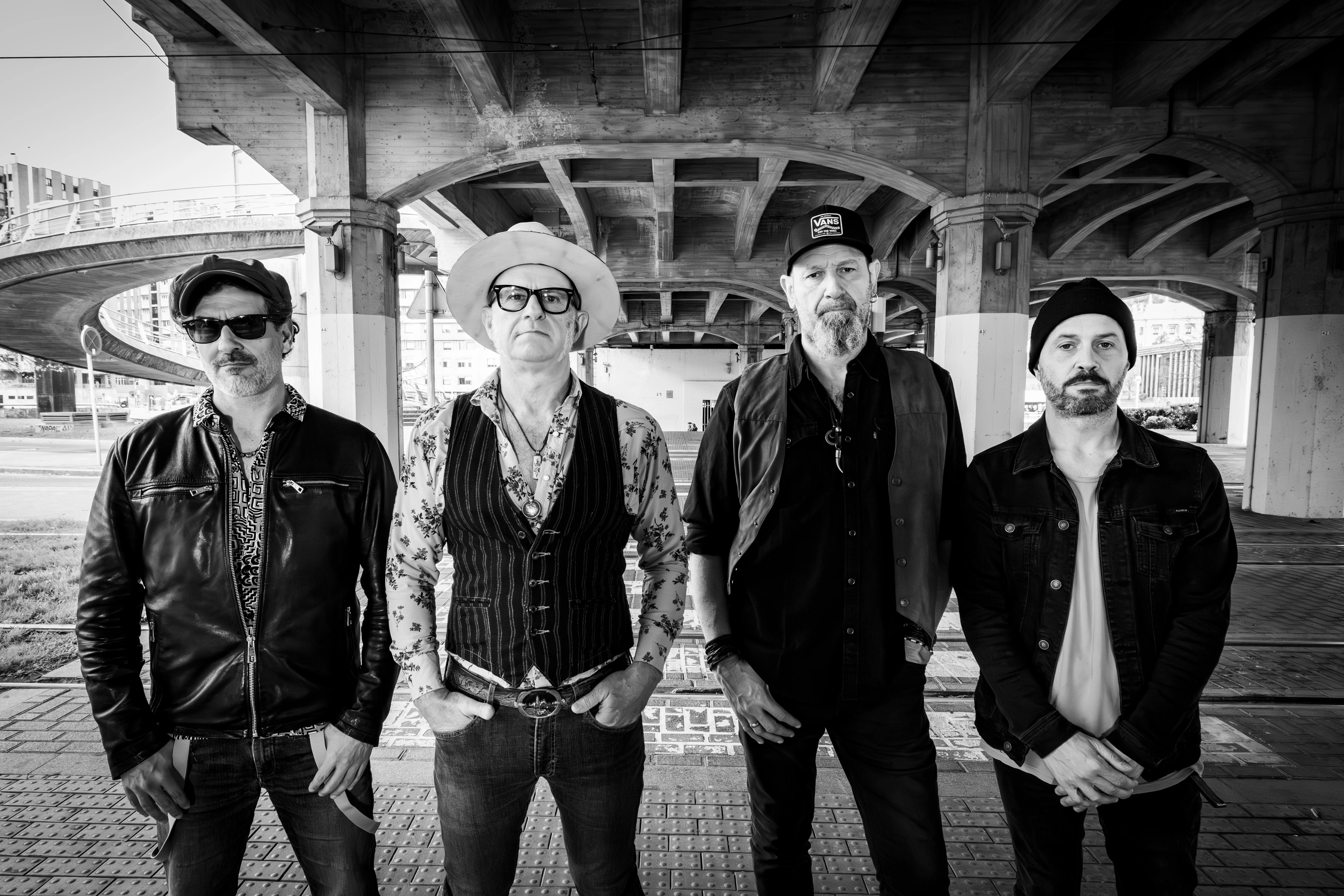 The four band members standing under a bridge, in black and white