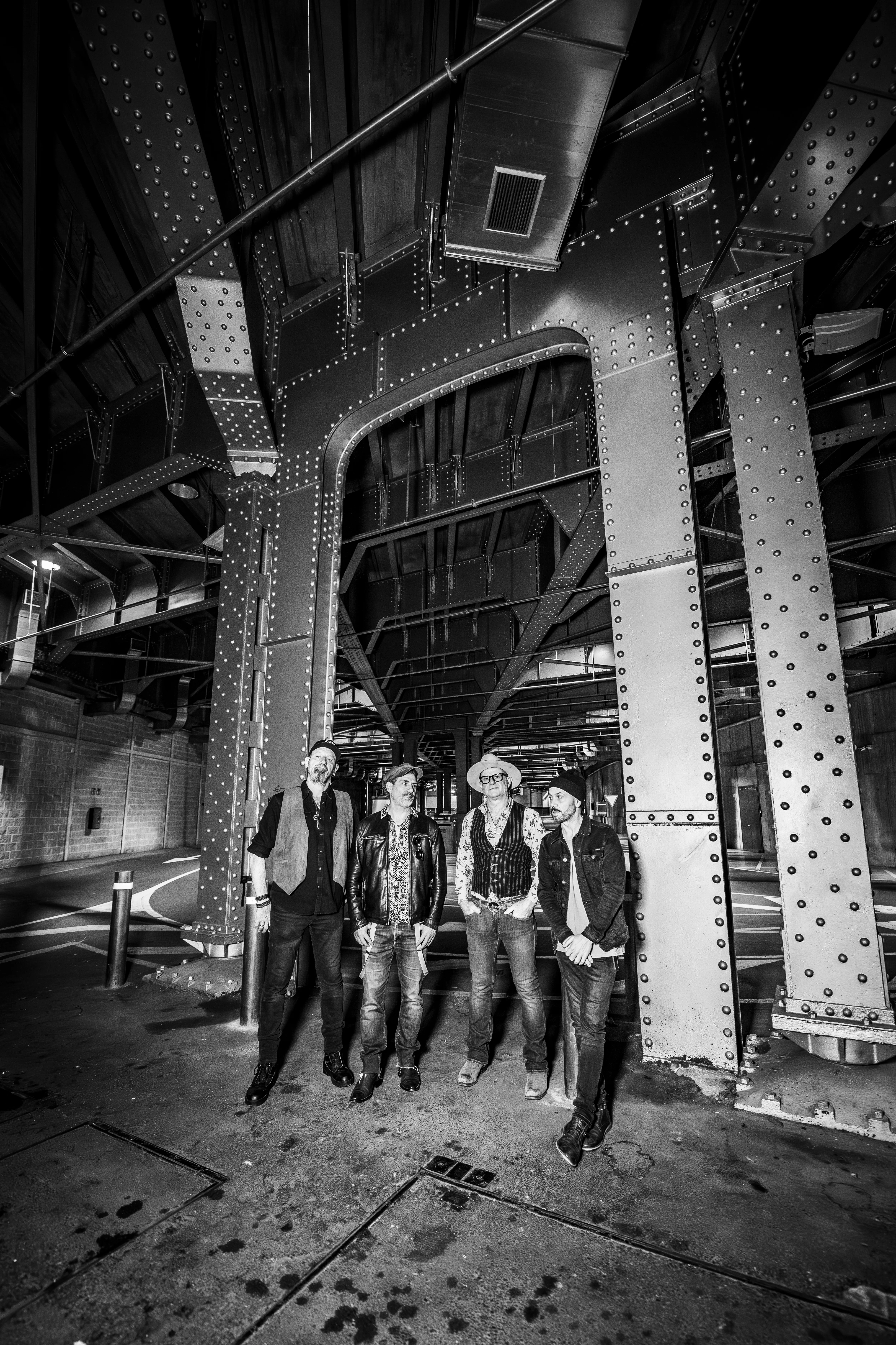 The band standing under an iron bridge, in black and white