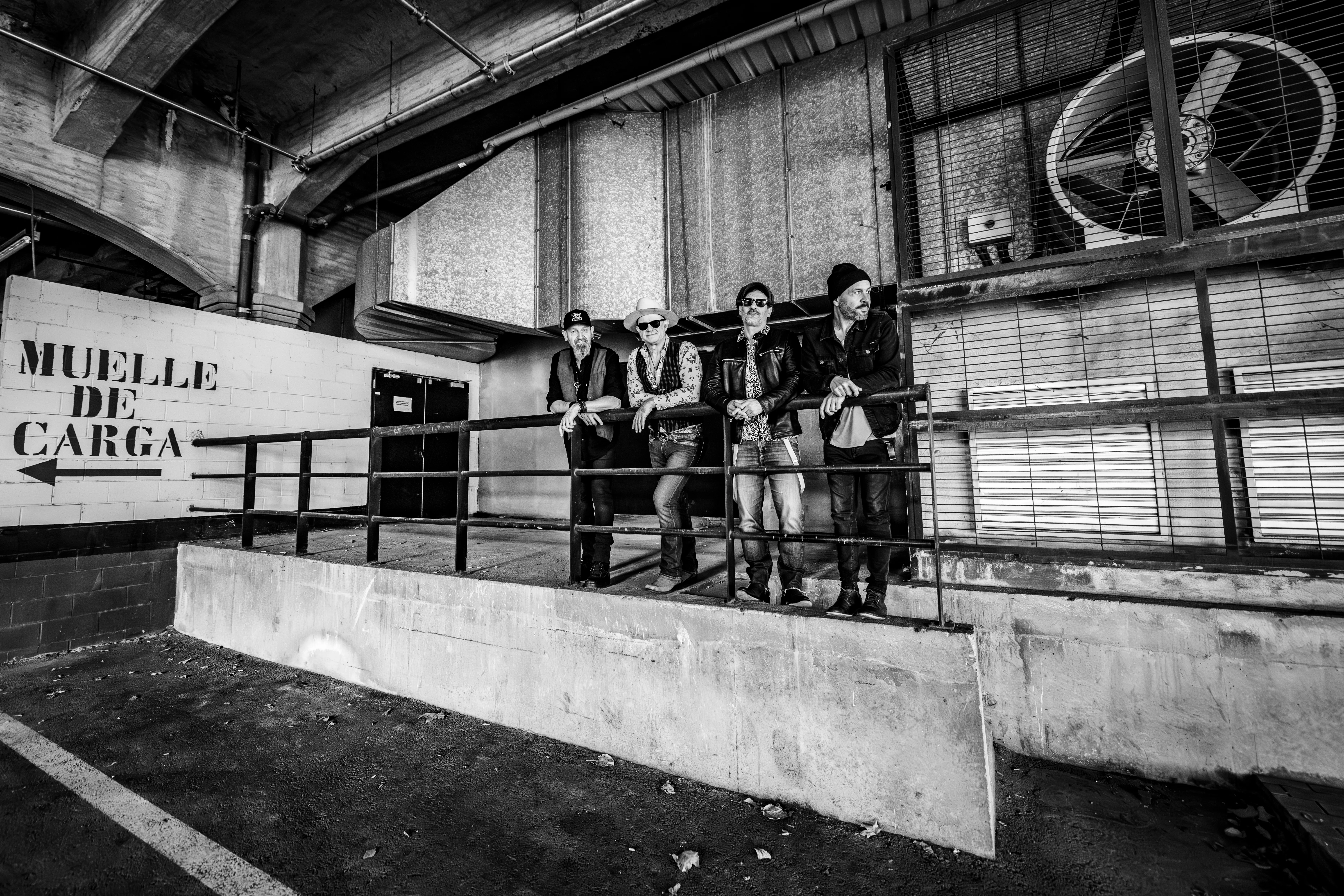 The band leaning on a railing at a loading dock, in black and white