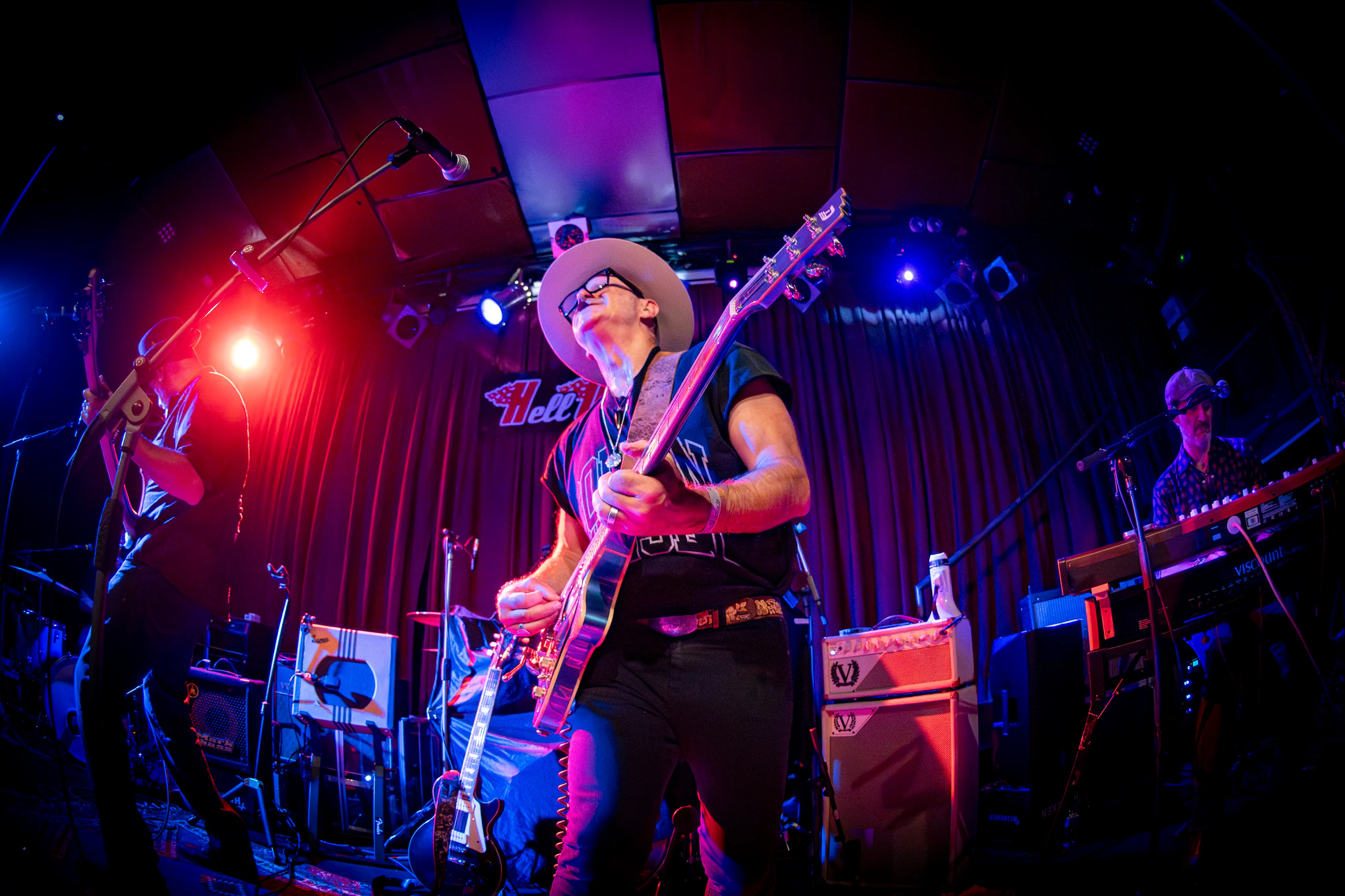 The guitarist in a white hat playing under red and blue stage lights